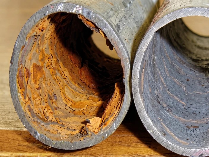 Mặt cắt đoạn ống nước cũ: lòng ống bám lớp cặn dày, cạnh một đoạn ống chưa bị bám